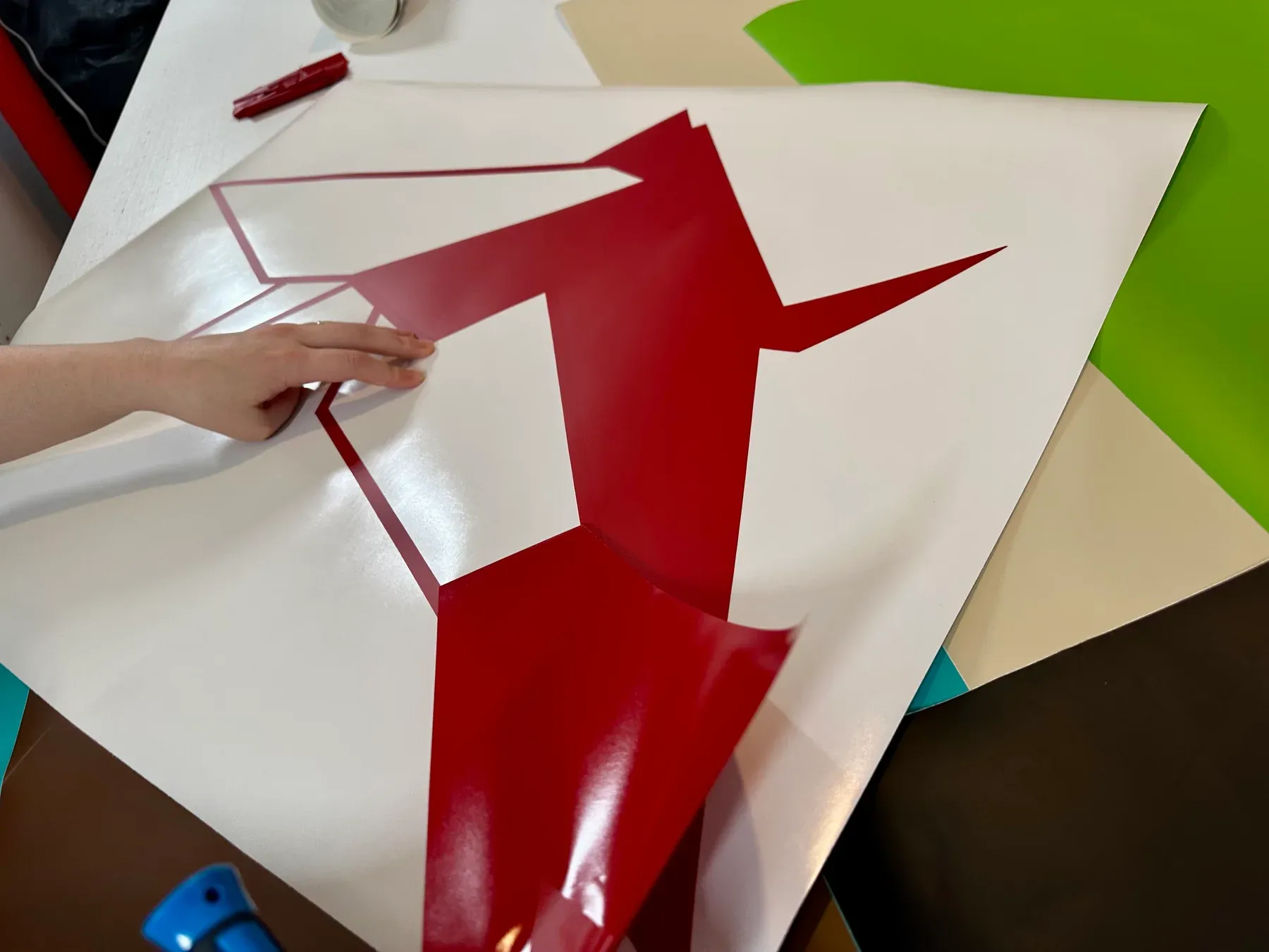 Uma mão retira o vinil vermelho à volta de um pássaro em origami no atelier Magic Stickers.