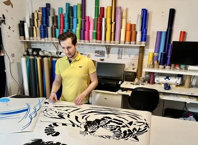Aymeric Wilke à l’atelier, devant des motifs découpés et les rouleaux d’adhésif coloré.